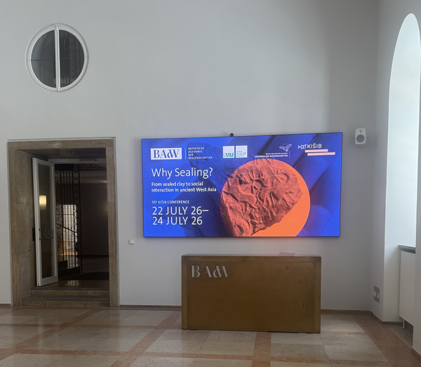 Blogpost_20260825_Teaserbild The foyer of the Bavarian Academy of Sciences and Humanities in the Residence of Munich showing the poster of the conference on a screen.